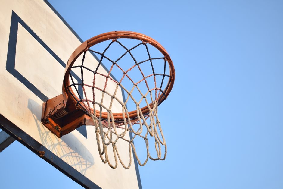 Close-up of a basketball hoop with net against a clear blue sky, perfect for sports themes.