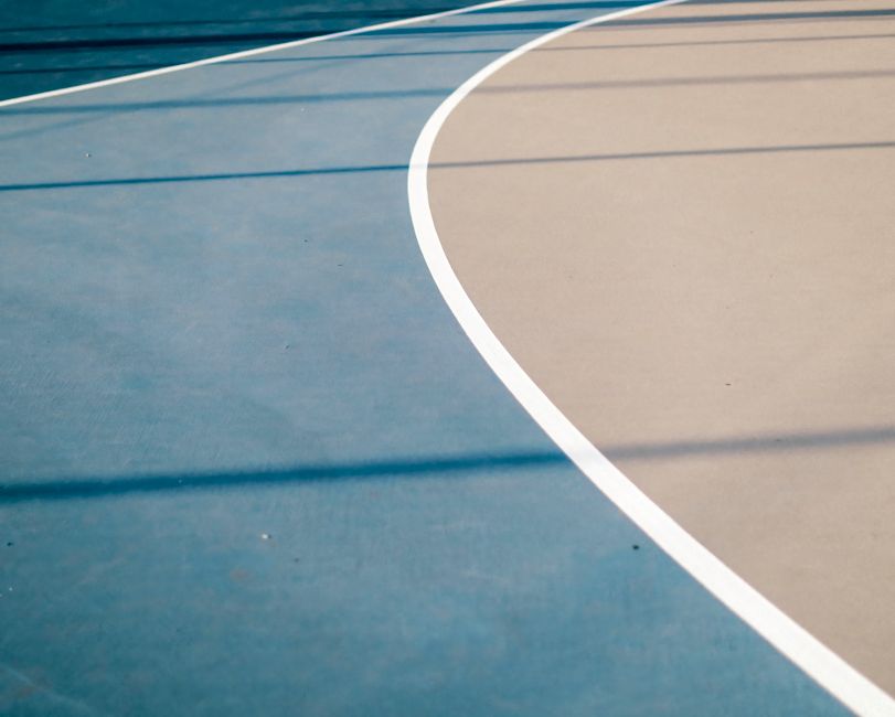 Close-up view of curved lines on an outdoor basketball court with blue and beige surfaces.